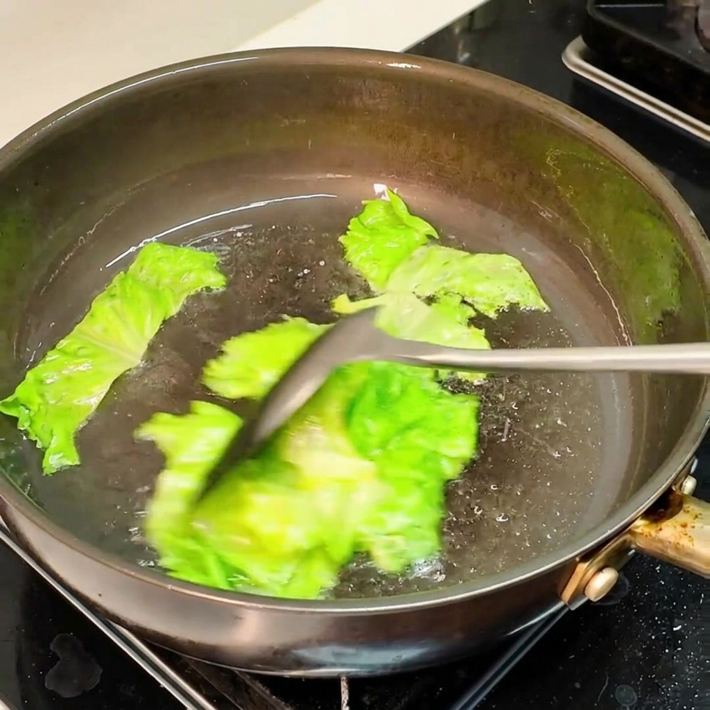 Morceaux de laitue verte sautés dans une poêle huilée et bien chaude avec une spatule.