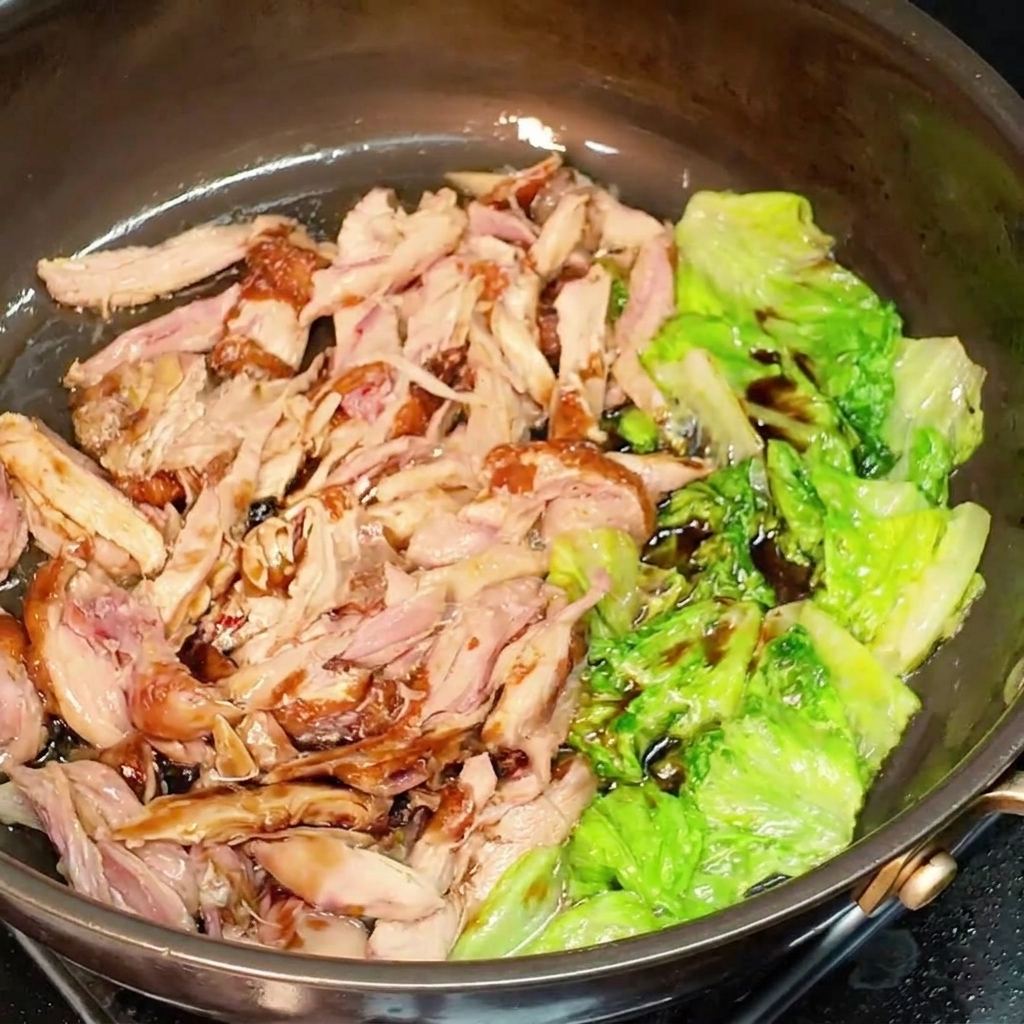 Poulet effiloché et laitue enrobés de sauce soja mélangés ensemble dans une poêle.