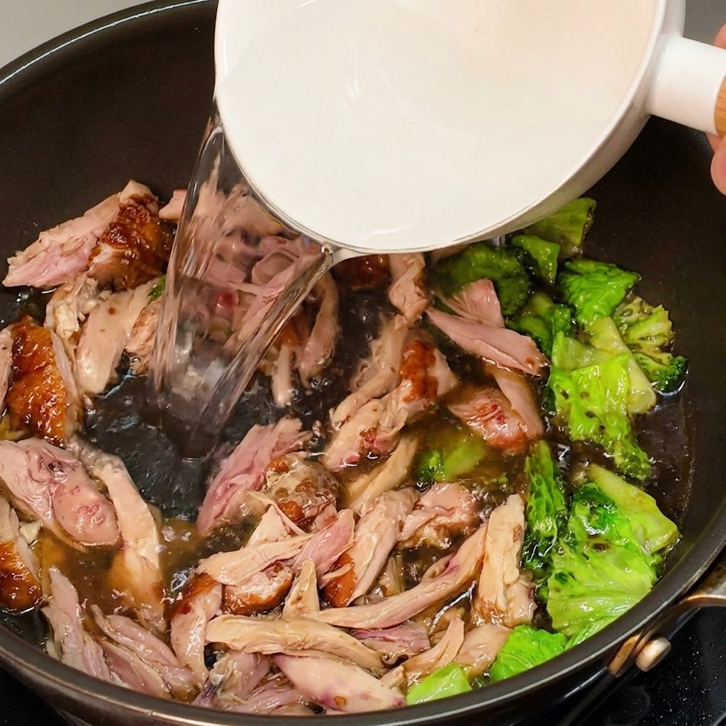 Eau très chaude versée dans une poêle contenant le poulet assaisonné et la verdure pour former le bouillon.