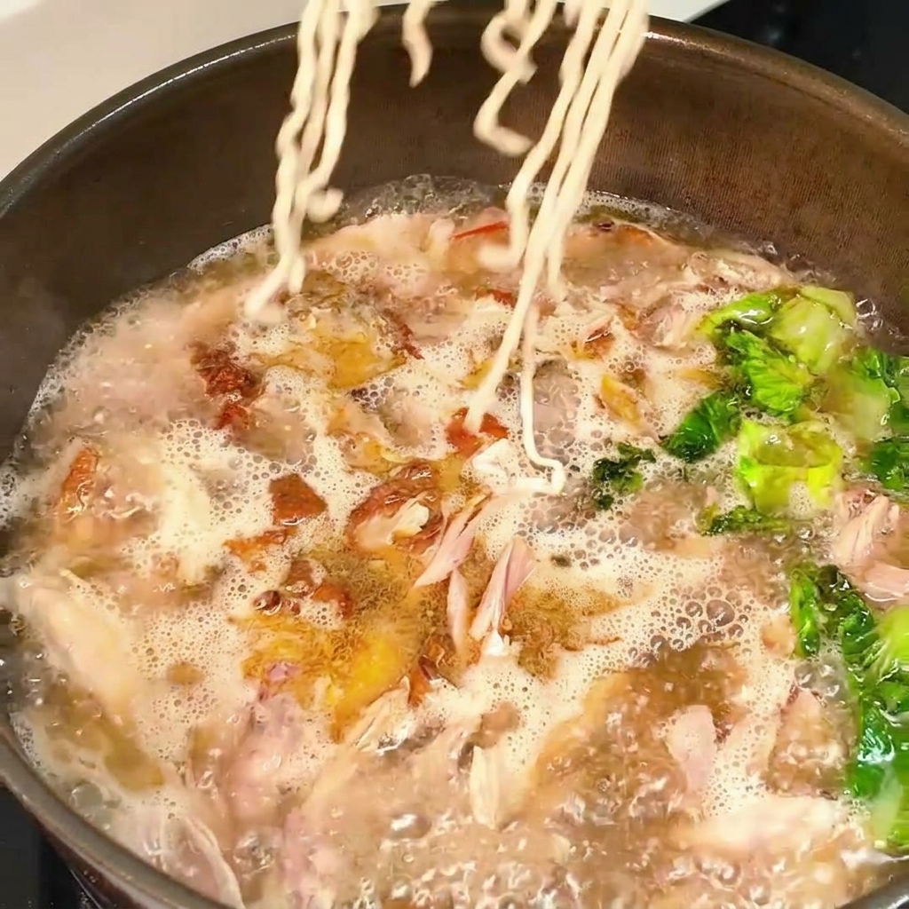 Un bloc de nouilles sèches plongé dans un bouillon bouillonnant au poulet et à la laitue.