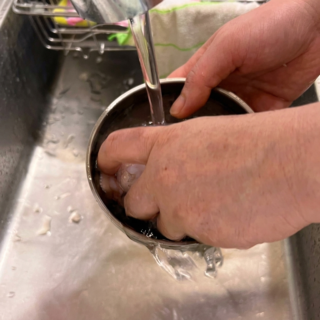 Des ailes de poulet fraîches rincées dans un bol en acier inoxydable sous un robinet de cuisine.