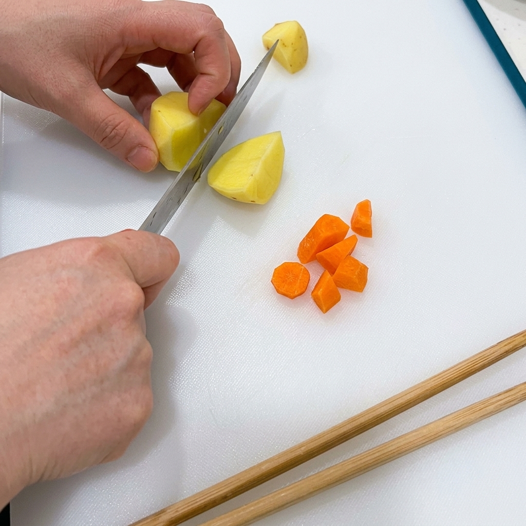 Des carottes et des pommes de terre coupées en petits dés sur une planche à découper blanche.