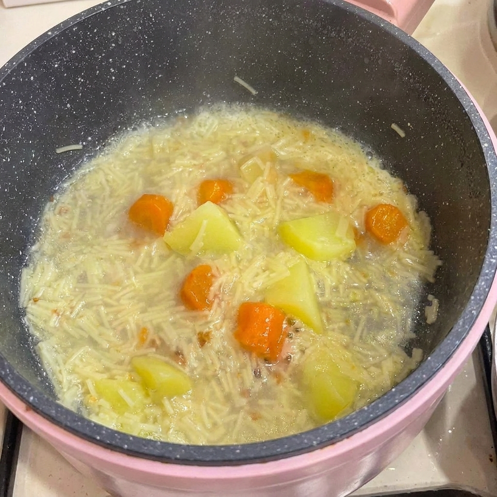 La viande de poulet désossée est ajoutée dans une casserole remplie de nouilles cuites, de pommes de terre et de carottes dans leur bouillon.