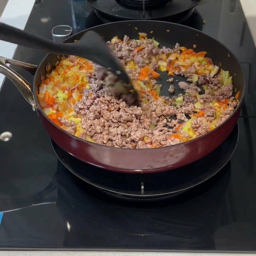 De la viande hachée et des légumes en dés mélangés ensemble dans une poêle avec une spatule noire.
