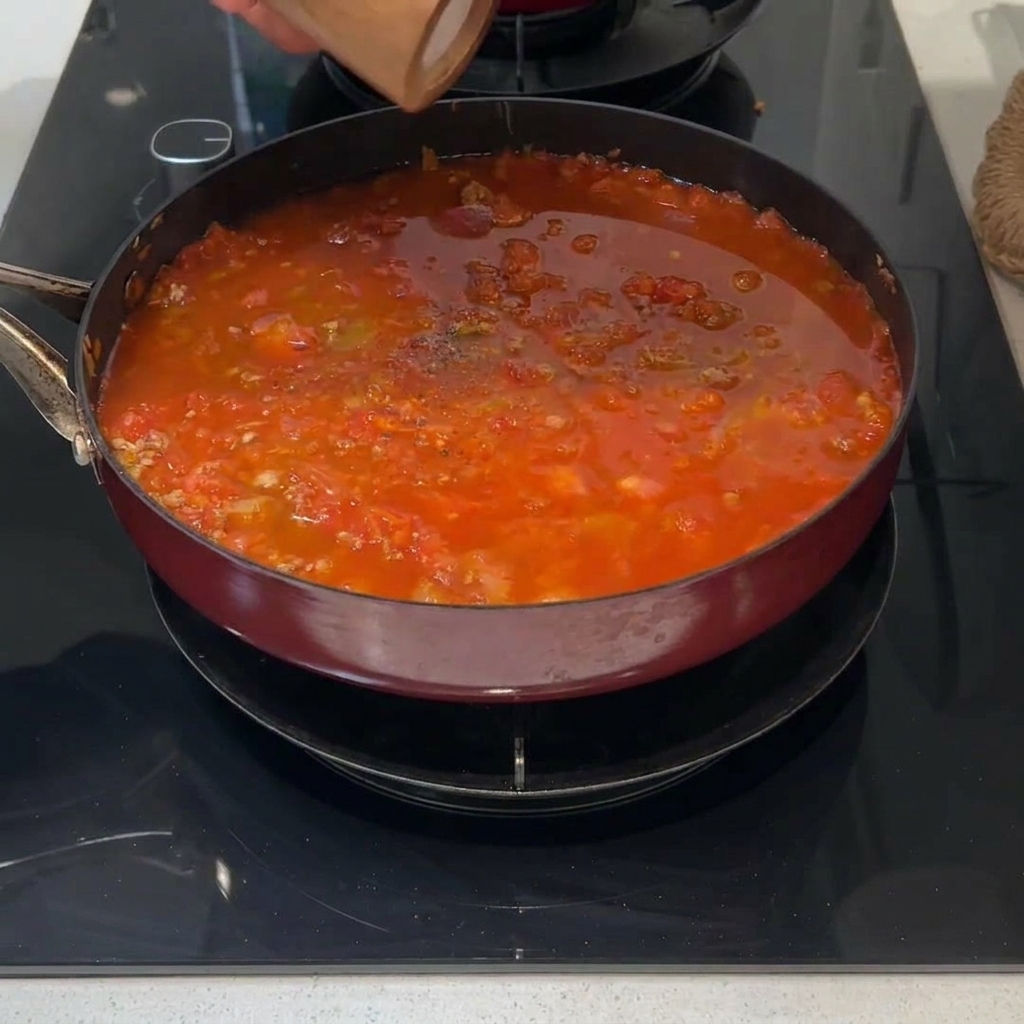 Une branche verte de romarin frais posée à la surface dune sauce à la viande rouge qui mijote.