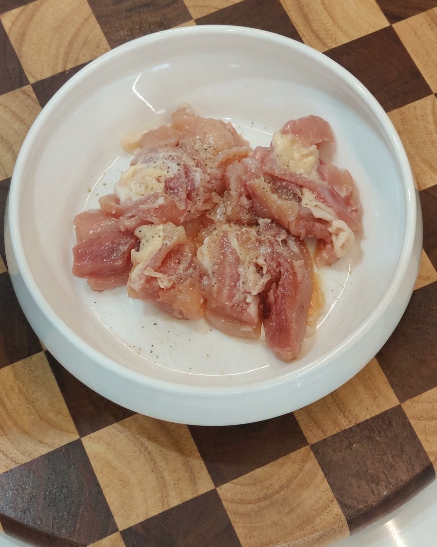 Bol contenant des morceaux de poulet crus assaisonnés, prêts pour la poêle.