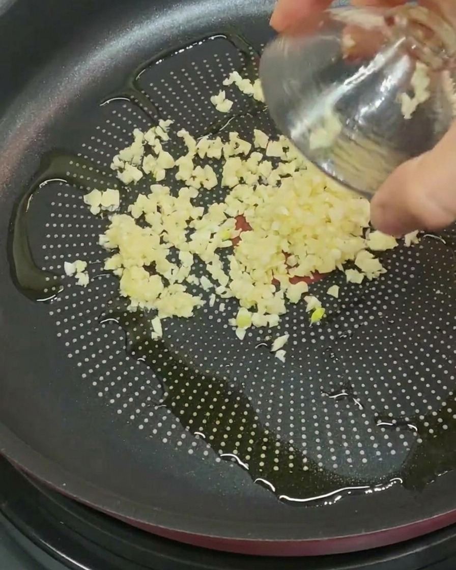 Ail haché versé dans une poêle avec de lhuile dolive.