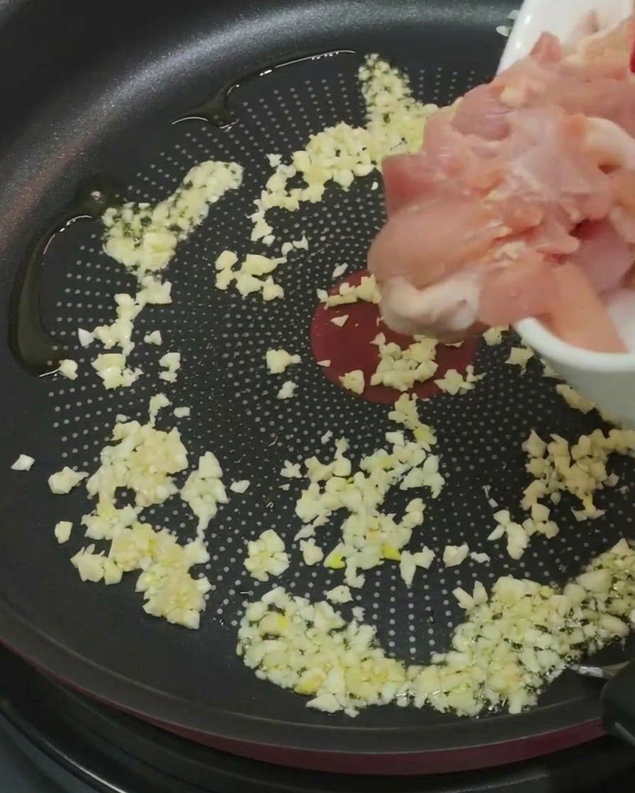 Morceaux de poulet ajoutés dans une poêle avec lail et lhuile.