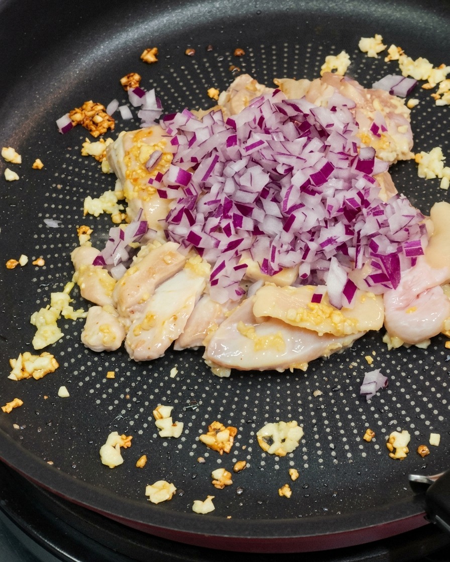 Dés doignon rouge ajoutés au poulet dans la poêle.