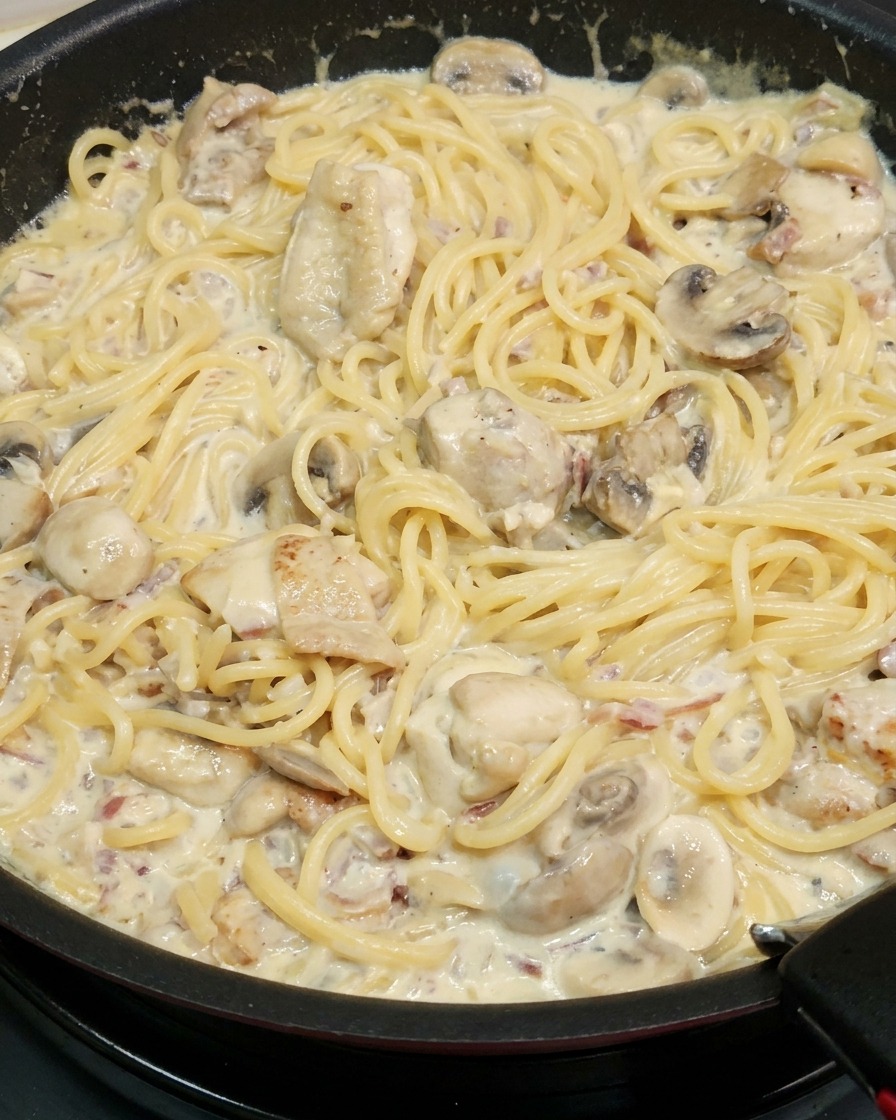 Spaghettis mélangés à la sauce épaissie et aux morceaux de poulet.