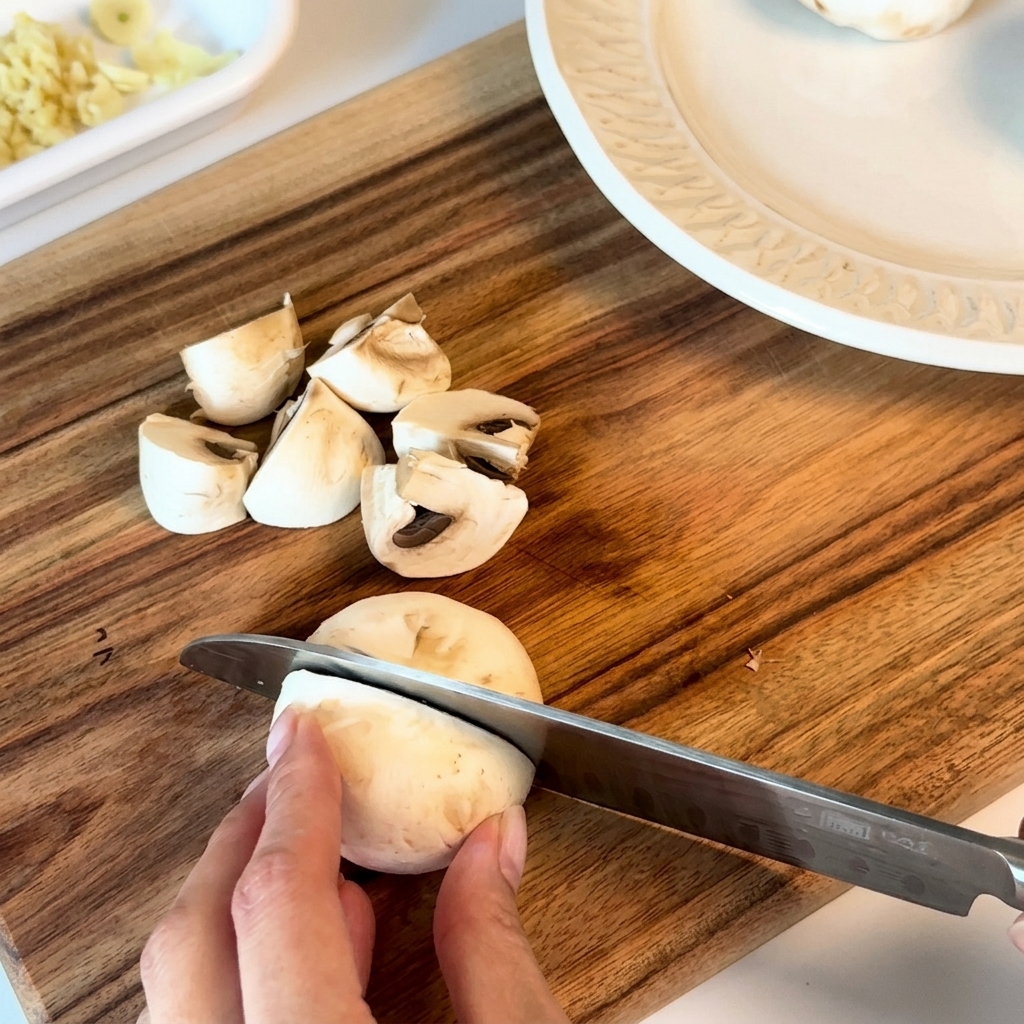 Champignons frais coupés en deux ou en quatre sur une planche en bois.