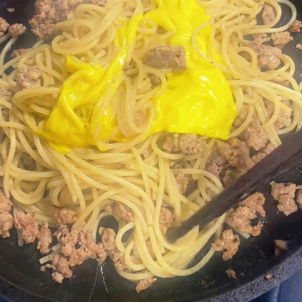 Le fromage fondu mélangé aux spaghetti et à la sauce à la viande dans la poêle.