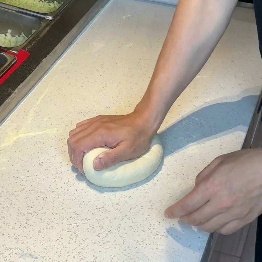 Mains pressant une boule de pâte à pizza sur un plan de travail blanc fariné.