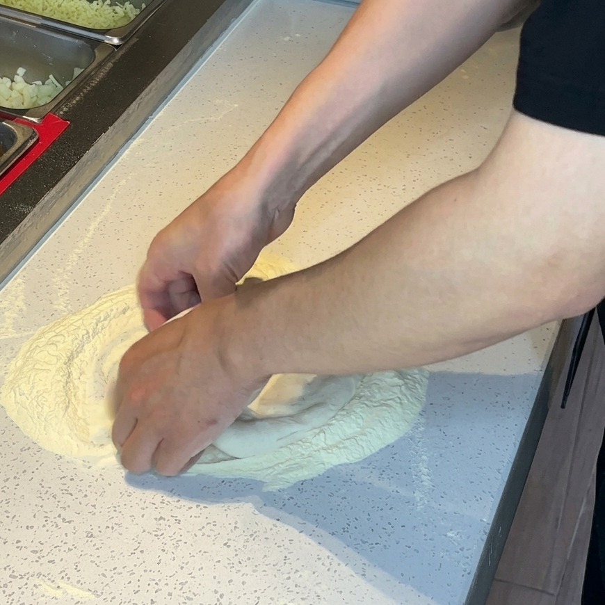 Mains pressant et étirant la pâte à pizza dans un tas de farine sur une surface blanche.