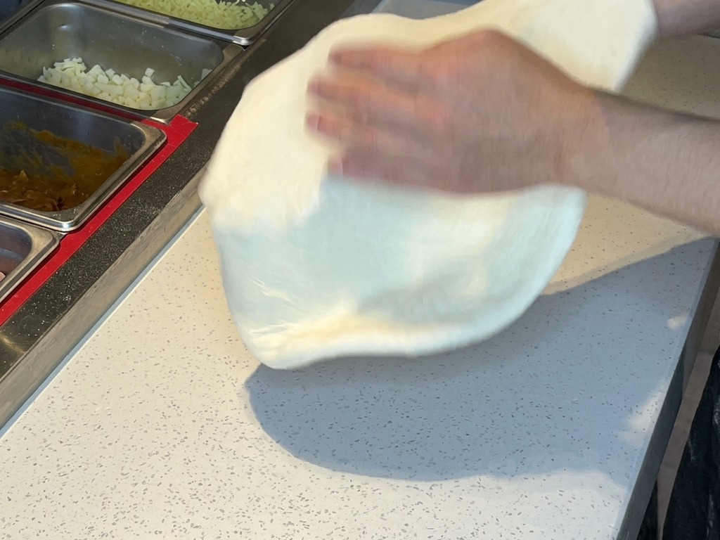 Deux mains soulevant et faisant passer la pâte à pizza étirée dune main à lautre pour enlever lexcédent de farine.