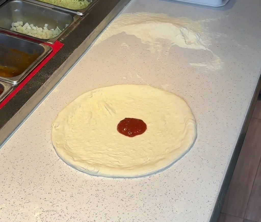 Une louche de sauce tomate rouge riche placée au centre dune croûte à pizza étirée.