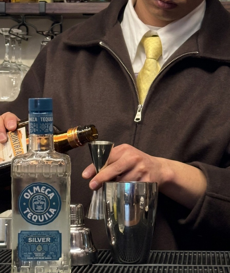 Du triple sec est versé depuis une bouteille dans un doseur positionné au-dessus dun shaker.