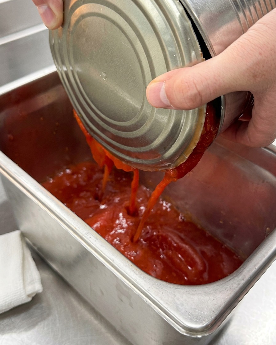 Tomates pelées en conserve versées dans un récipient en acier inoxydable.