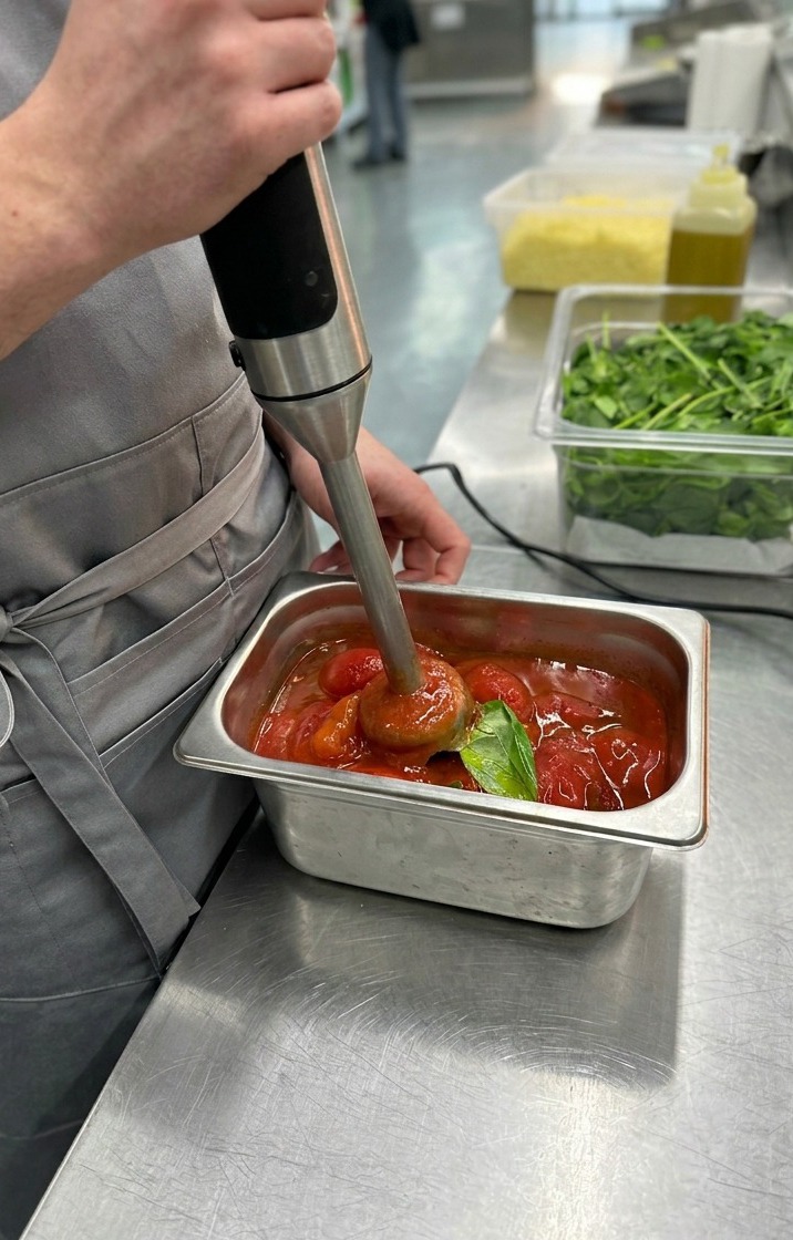 Mixeur plongeant transformant les tomates et le basilic en une sauce rouge lisse.