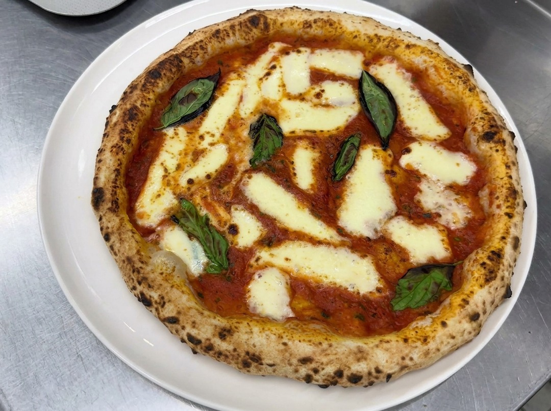 Mains étirant délicatement une boule de pâte à pizza sur un plan de travail fariné.