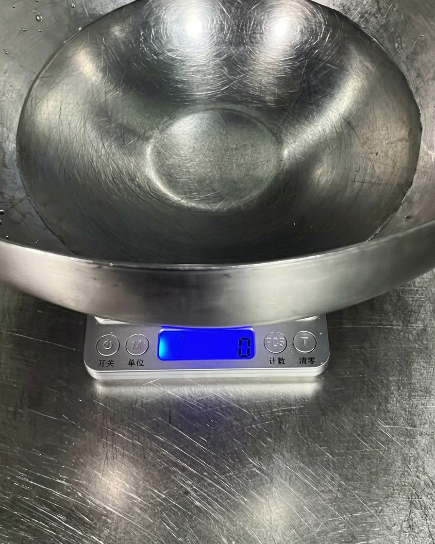 Un grand bol en inox rempli deau claire sur une balance de cuisine numérique.