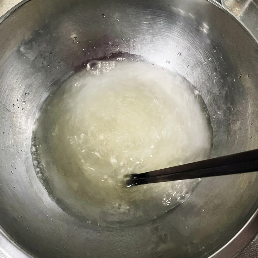 Des baguettes mélangeant le mélange deau, levure et sel dans un grand bol en métal.