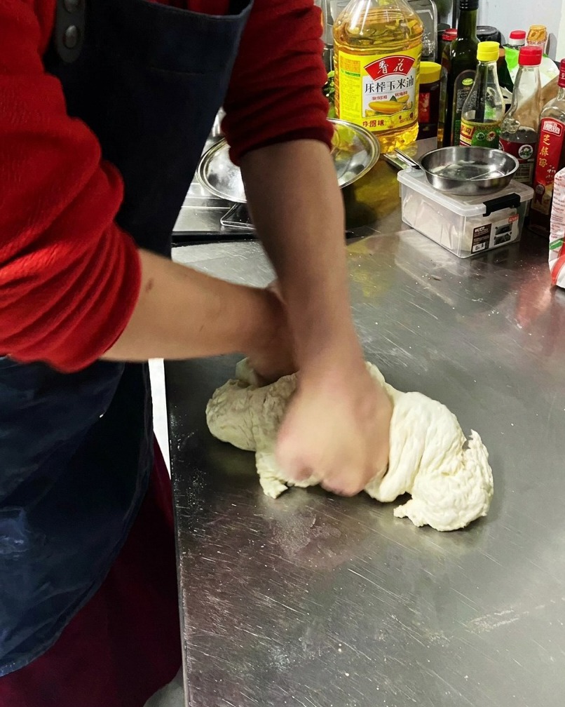 Gros plan sur la pâte pétrie sur une surface en inox, montrant une texture élastique.