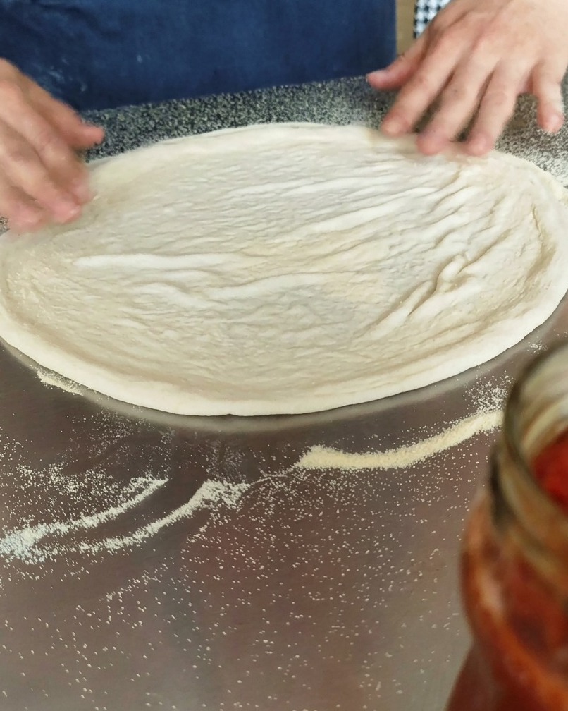 Pâte à pizza circulaire posée sur un plan de travail fariné à la semoule.