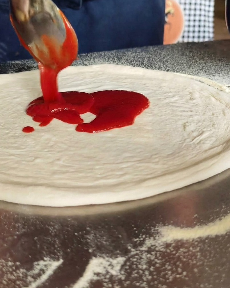 Sauce tomate étalée en cercle au centre de la pizza.