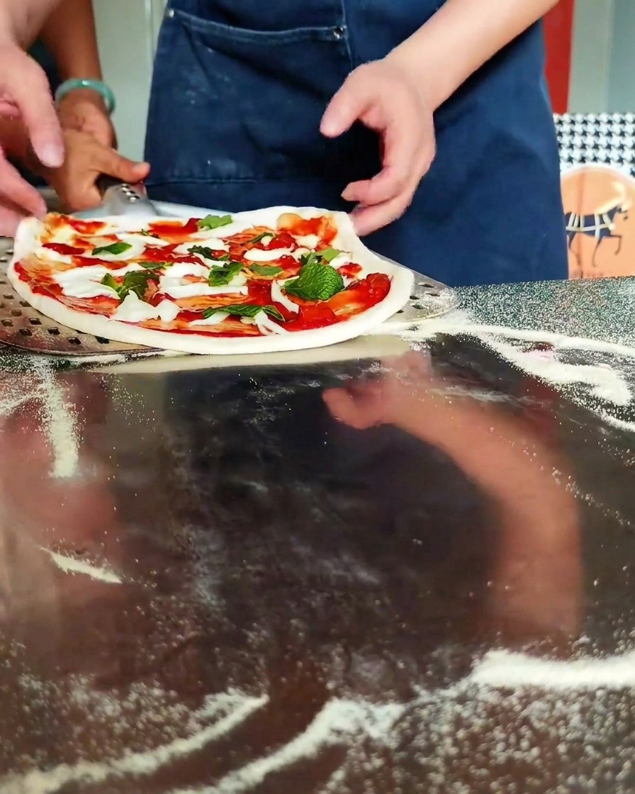 Mains positionnant la pizza sur une pelle perforée.
