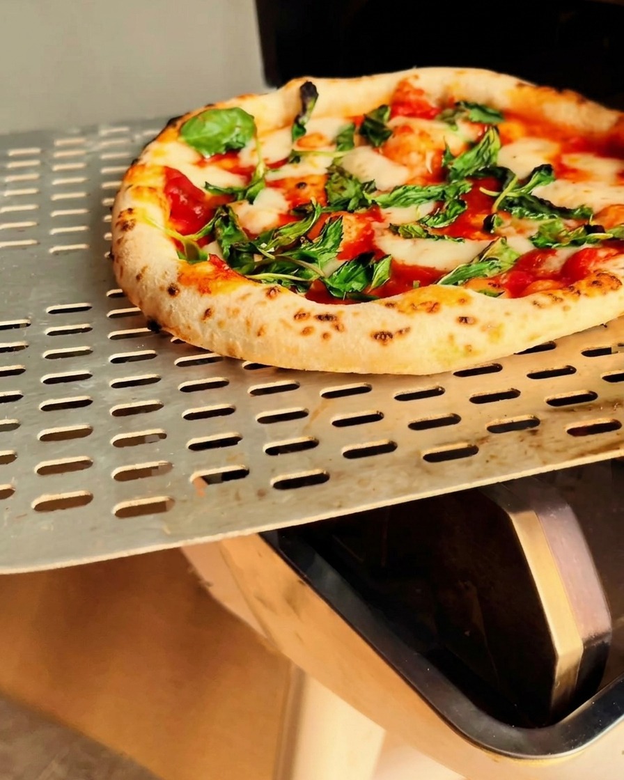 Pizza Margherita tout juste cuite sortie du four sur une pelle en métal.