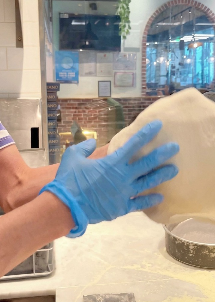 Pâte à pizza lancée et étirée dans lair par des mains gantées de bleu.