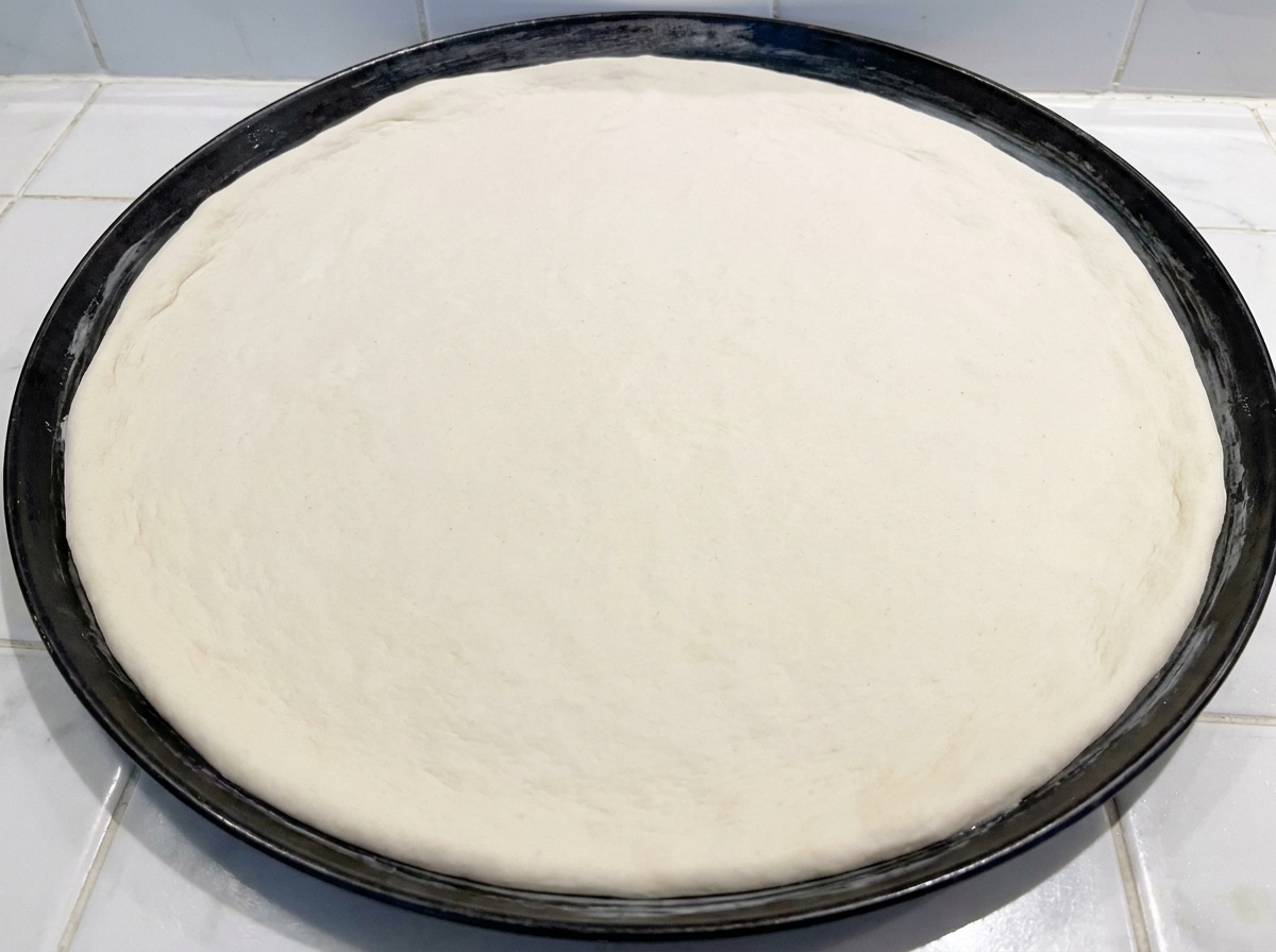 Un disque de pâte à pizza crue pressé dans un moule à pizza noir.