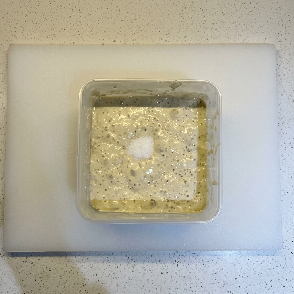 Du sel et un tas de farine sur une pâte fermentée pleine de bulles dans un récipient carré.