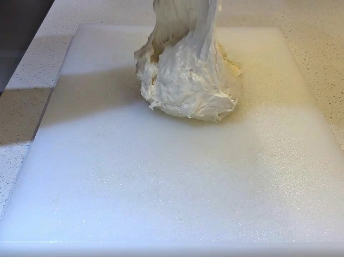 Une pâte molle et collante déposée sur une planche à découper blanche huilée.