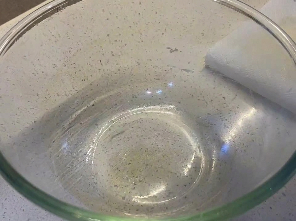 Une boule de pâte à pizza ronde et lisse reposant dans un grand bol en verre légèrement badigeonné dhuile.