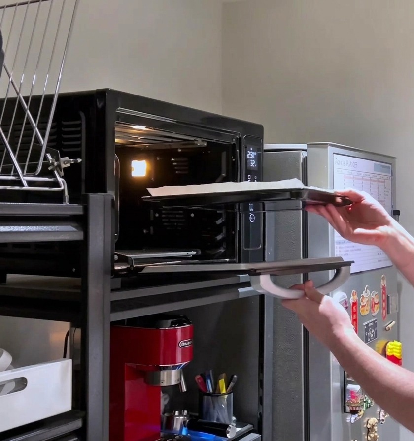 Une personne remettant la pizza rectangulaire richement garnie de fromage dans le four chaud pour sa cuisson finale.