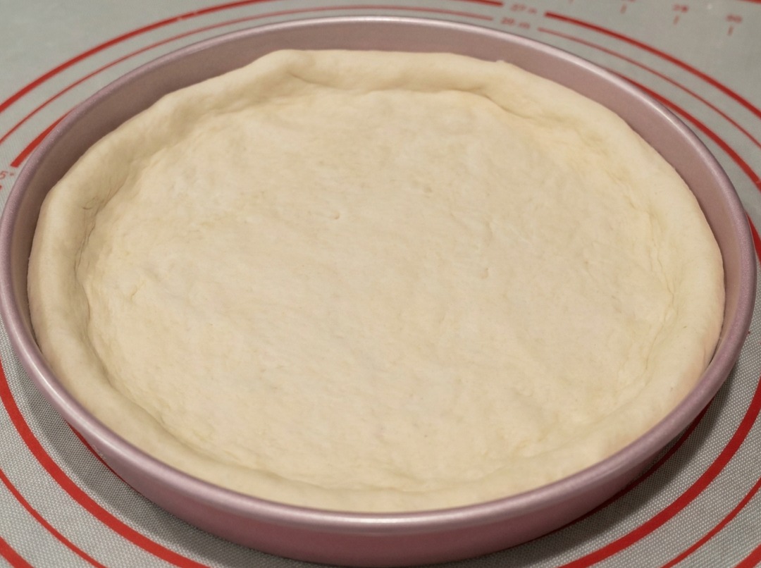 La pâte est placée dans un moule à pizza en métal de 23 cm, avec les bords façonnés à la main.