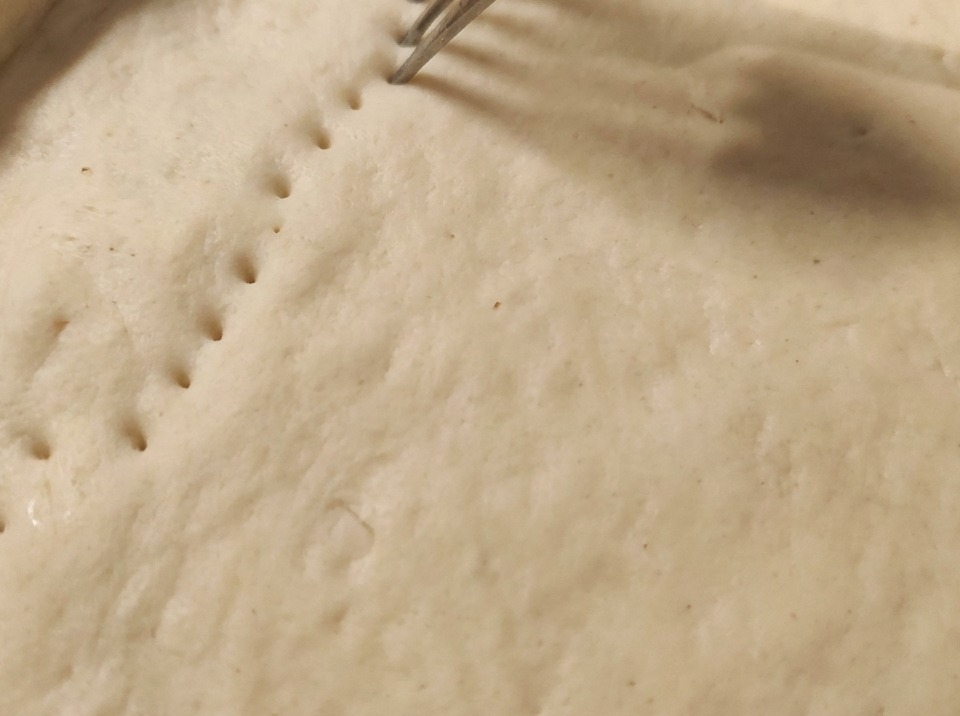 Une fourchette enfoncée dans la pâte crue pour créer des rangées de trous sur la surface.