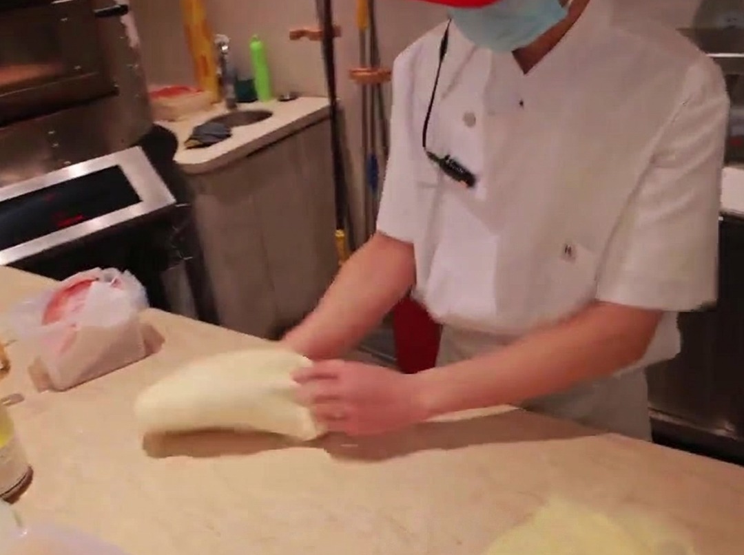 Les mains dun chef étalant une boule de pâte à pizza sur un plan de travail en marbre fariné.