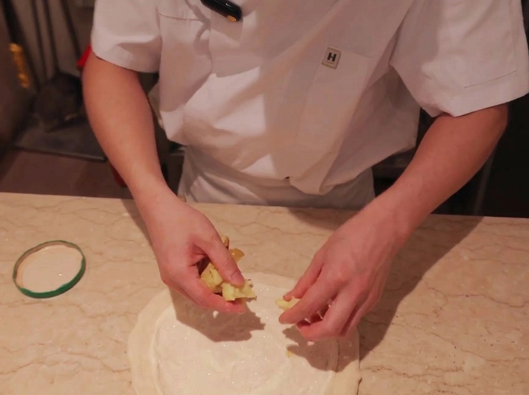 Des tranches fines de pommes de terre déposées sur une base de pizza recouverte de sauce.