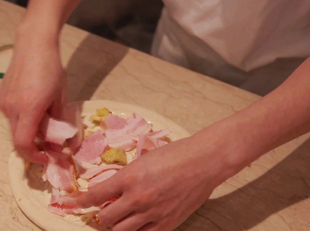 Des tranches de porc délicatement disposées sur les pommes de terre garnissant la pâte à pizza.