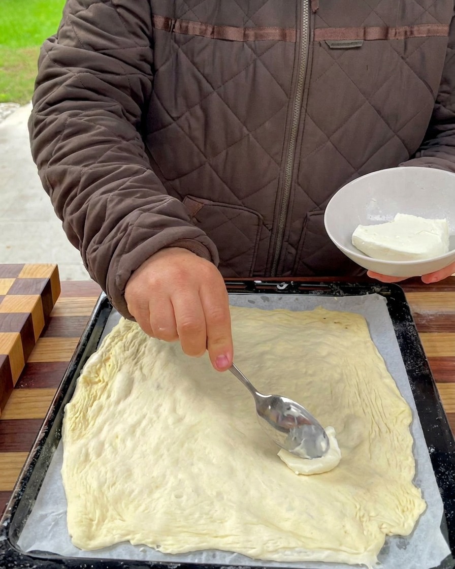 Base de fromage crémeux étalée à la cuillère sur la surface de la pâte à pizza.