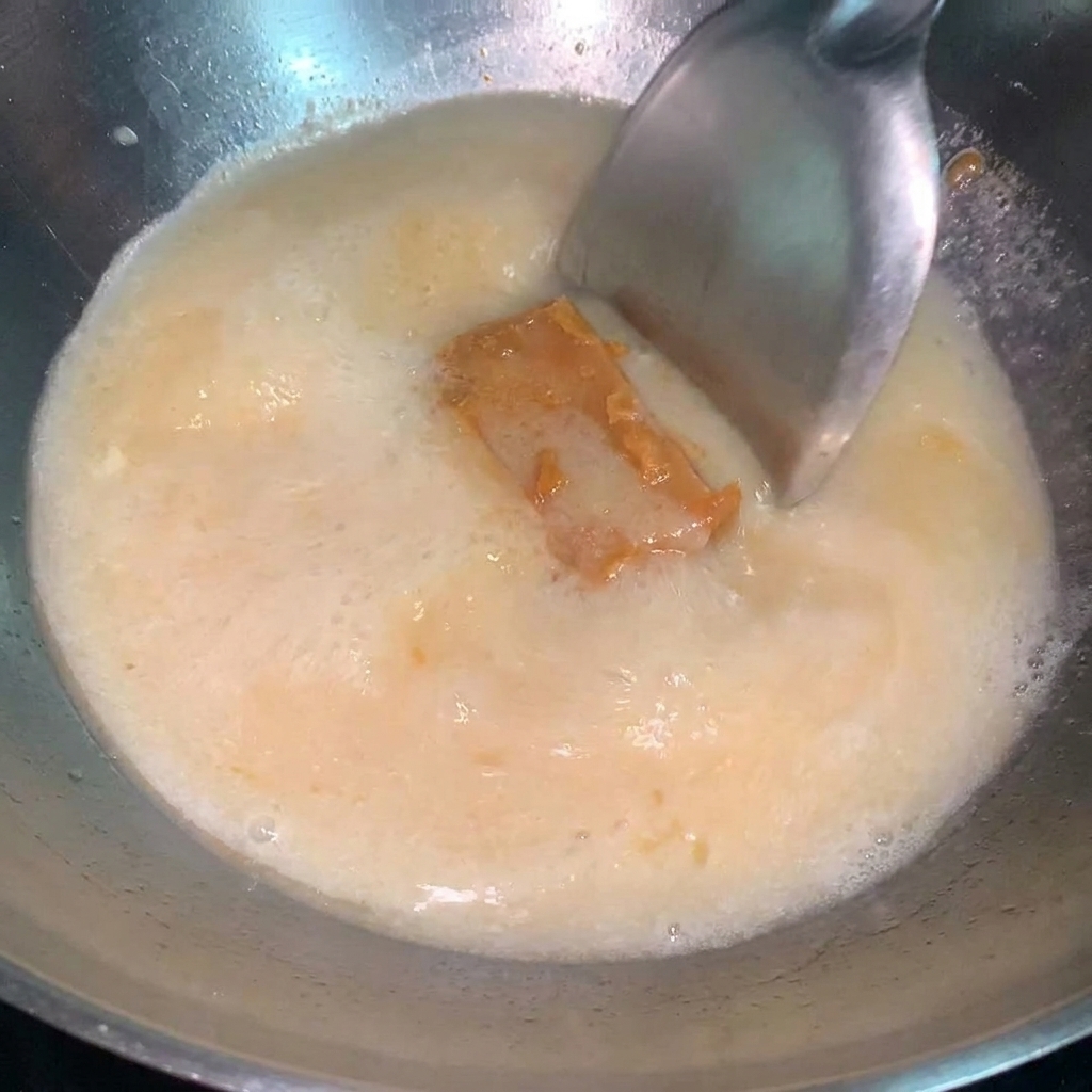 Une cuillerée de sauce miso concentrée incorporée dans une casserole de bouillon de ramen frémissant.