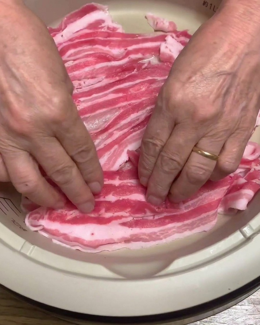 Gros plan sur des tranches de poitrine de porc crue soigneusement disposées au fond dune casserole électrique.