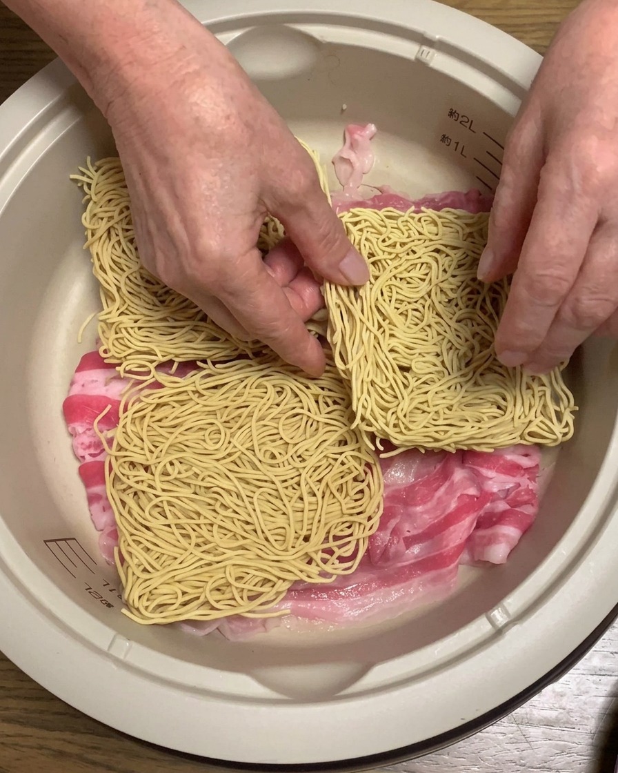 Blocs de nouilles ramen sèches déposés sur la couche de porc à lintérieur de la casserole.