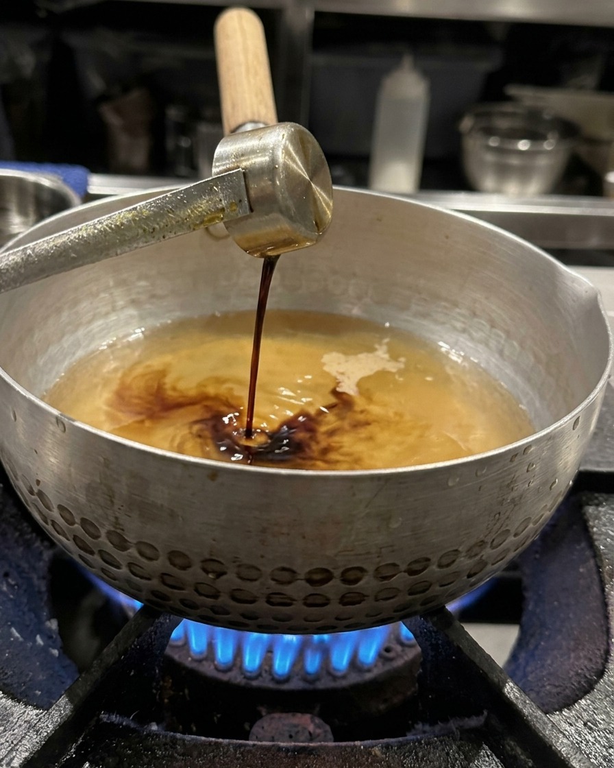 De la sauce soja versée dune louche en métal dans le bouillon frémissant, prête à être fouettée.