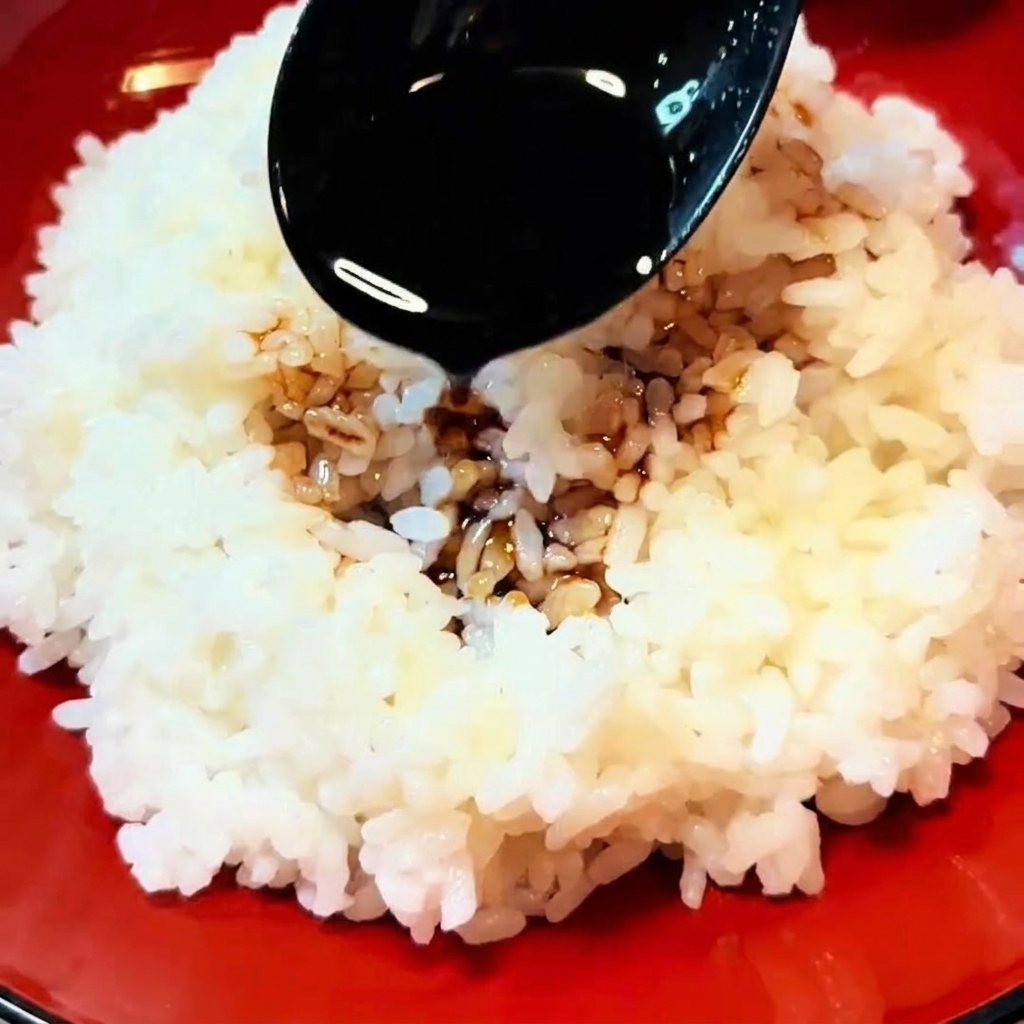 Une cuillère noire versant de la sauce brun foncé sur un bol de riz blanc fumant.