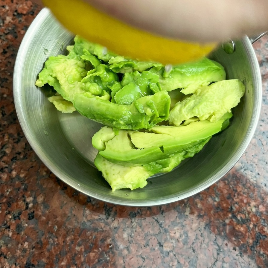 Du jus de citron frais pressé à la main sur des moitiés davocat dans un bol en inox.