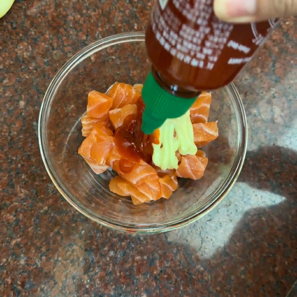 Des dés de saumon mélangés à une sauce onctueuse couleur orange dans un récipient en verre.